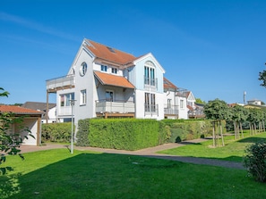 Une grande maison à deux étages, avec un toit recouvert de tuiles rouges, de nombreux balcons et un jardin bien entretenu.
