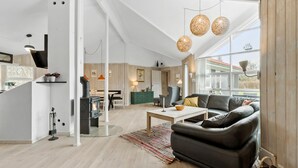 Un salon moderne doté d’une cheminée, d’un canapé, d’un coin repas et de grandes fenêtres offrant une vue sur l’extérieur.