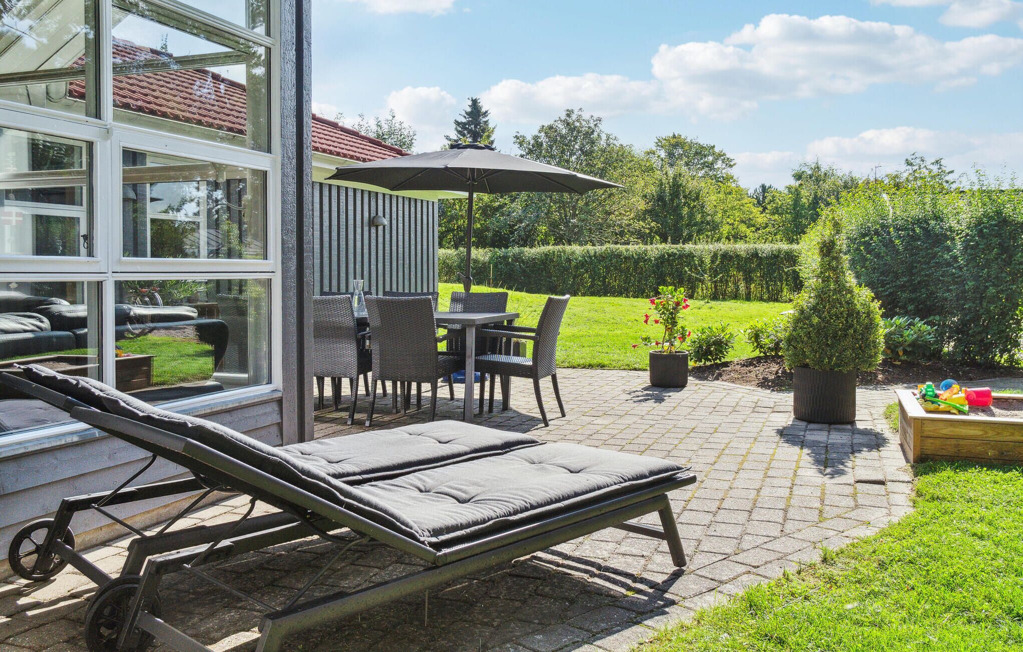 Une terrasse avec un transat, une table et des chaises d’extérieur, ainsi qu’un petit coin jardin agrémenté de plantes en pot.