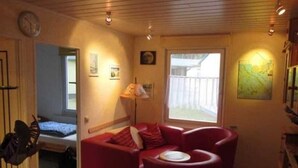 Ein gemütliches Wohnzimmer mit einem roten Sofa, einem kleinen Tisch und einem Fenster mit Blick auf eine Ziegelmauer.