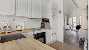 Ett modernt kök med vita köksskåp, en inbyggd ugn, en mikrovågsugn och en kaffemaskin.
