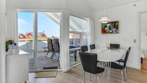 Ett modernt matområde med ett vitt bord och svarta stolar, stora fönster och en tavla på väggen.