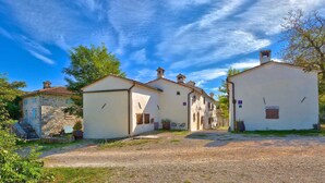 A row of white buildings with a gravel path in front, a stone building to the left, and a sign indicating a rental property. - Holiday home with terrace and barbecue (Buzet)