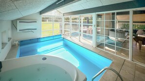 Una piscina interior con hidromasaje, ventanas amplias y vistas al exterior.
