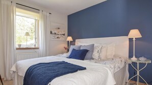 A bedroom with a bed, two bedside lamps, a window with curtains, and a wall with a painting.