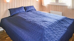 Ein Bett mit blauer, gemusterter Bettdecke in einem Zimmer mit Holzwänden und zwei Wandleuchten.