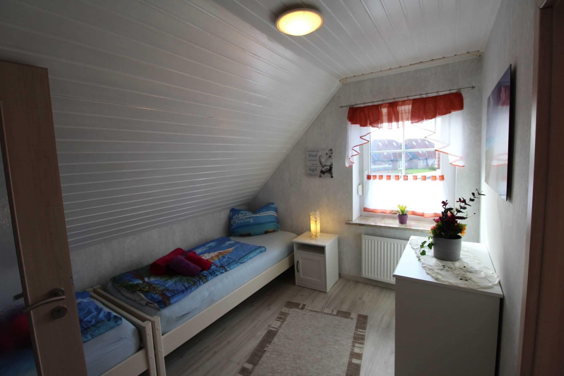 Ein kleines, gemütliches Schlafzimmer im Dachgeschoss mit Etagenbett, Schreibtisch und einem Fenster mit Vorhängen.
