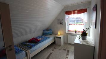 Ein kleines, gemütliches Schlafzimmer im Dachgeschoss mit Etagenbett, Schreibtisch und einem Fenster mit Vorhängen.