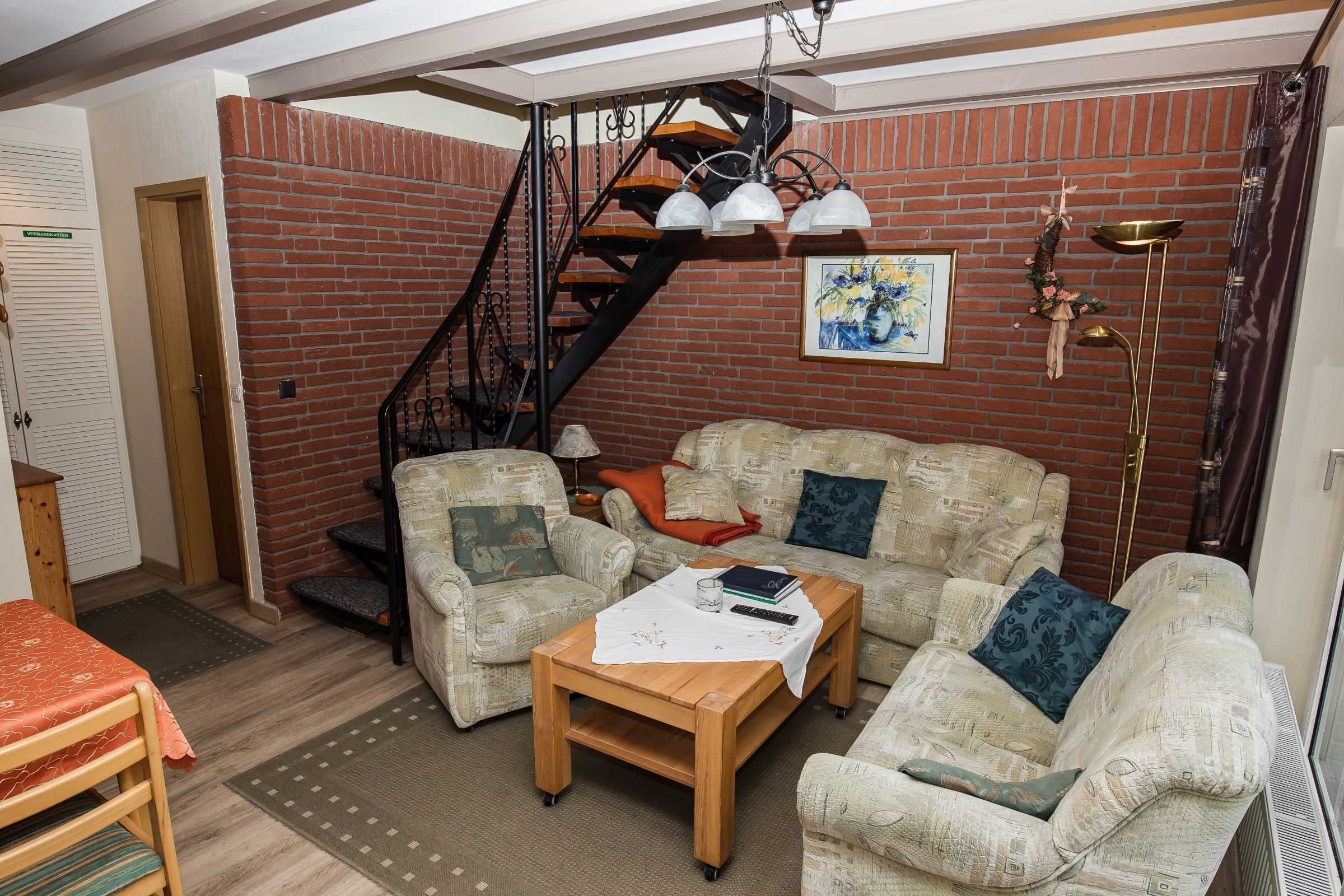 Un salon chaleureux avec un mur en briques, un escalier en bois, un ensemble de canapés, une table basse et un lampadaire.