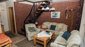 Un salon chaleureux avec un mur en briques, un escalier en bois, un ensemble de canapés, une table basse et un lampadaire.