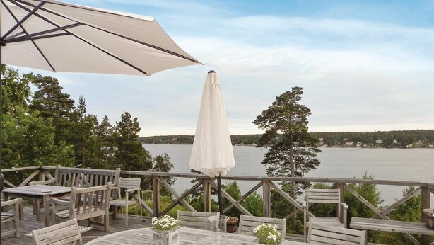 Una terraza de madera con mobiliario exterior, una sombrilla blanca y vistas a un lago.