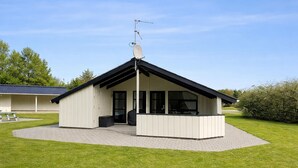 A small, single-story building with a sloped roof and a satellite dish. It has a covered patio area with a bench and a trash bin. - Nice home in Oksbøl with sauna (Oksbøl)