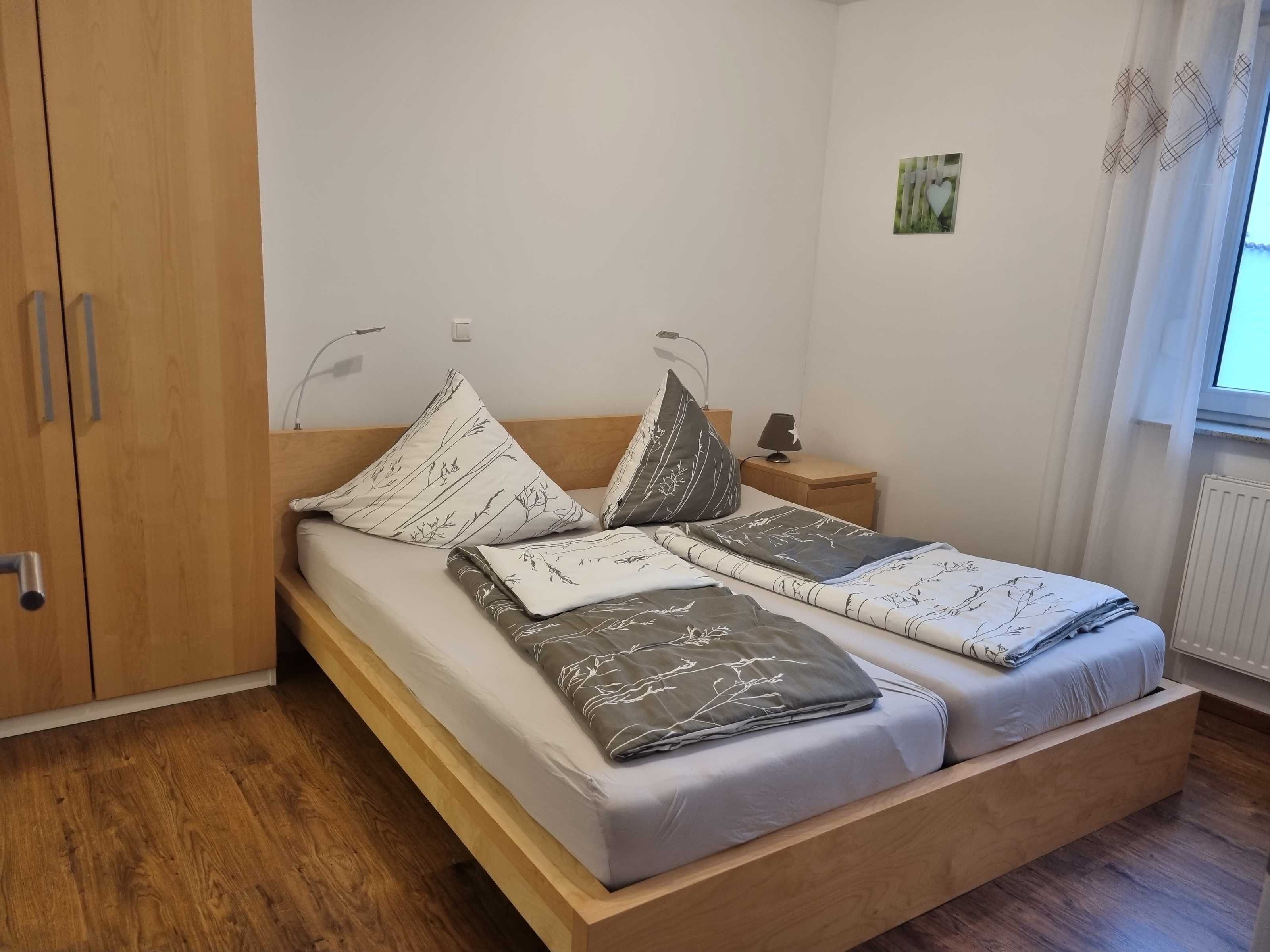 A single bed with a wooden frame, a bedside table with a lamp, and a wall-mounted light fixture.