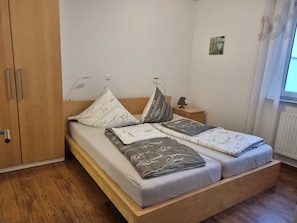 Un lit simple avec un cadre en bois, une table de chevet avec une lampe et un luminaire fixé au mur.