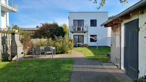 A modern two-story house with a patio, a barbecue grill, and a wooden fence. - Earth - house four elements holiday home with four apartments (Zinnowitz)