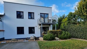 A modern two-story building with a flat roof, numbered 22, featuring a balcony with metal railings and a small outdoor seating area. - Earth - house four elements holiday home with four apartments (Zinnowitz)