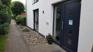 A modern building with a dark door, a small garden area with rocks and potted plants, and a pathway leading to the entrance. - Earth - house four elements holiday home with four apartments (Zinnowitz)
