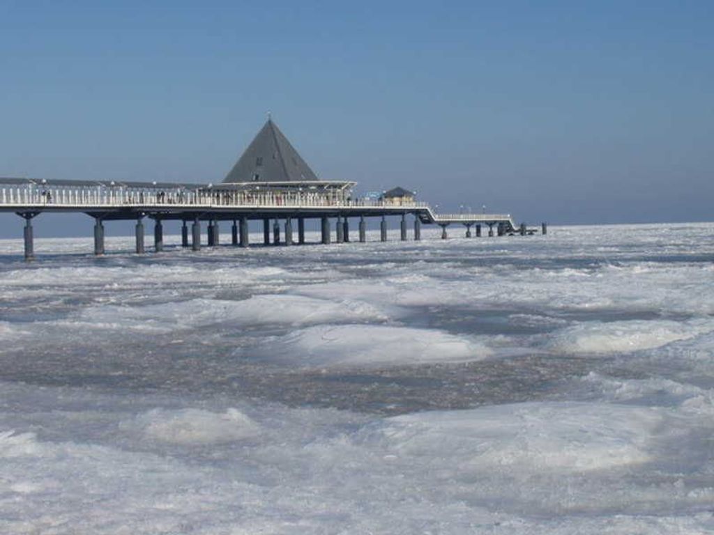 Un muelle se adentra en una masa de agua helada, con un edificio al final.