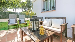 Un patio esterno con tavolo in legno, due poltrone imbottite, una divanetto in legno e due lanterne.