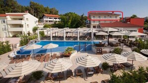 A pool area with lounge chairs and umbrellas, surrounded by buildings. - Holiday apartment with balcony and sea view (Klimno)