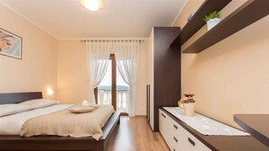 A bedroom with a bed, bedside tables, a dresser, and a window with curtains. - Holiday apartment with balcony and sea view (Klimno)