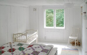 Una stanza con un letto, una culla, una sedia e una finestra vista verde.