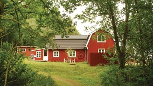 A red wooden house with a thatched roof, surrounded by lush greenery and a dirt path leading to it. - 3 bedroom awesome home in Mårdaklev (Mårdaklev)