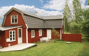 Una casa rossa con tetto spiovente, un patio in legno e un piccolo giardino.