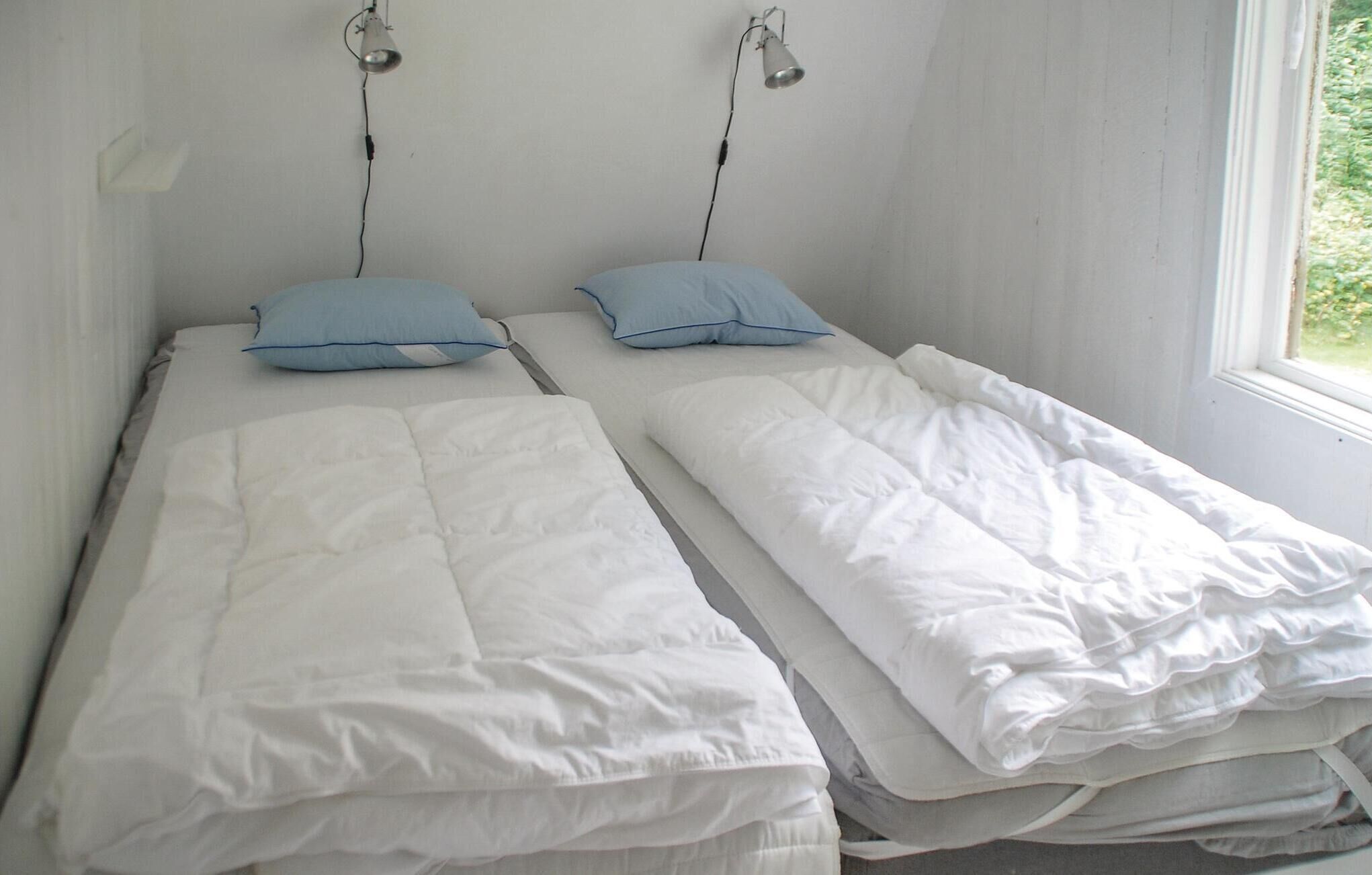 Twee eenpersoonsbedden met wit beddengoed en blauwe kussens in een kamer met witte muren en een raam.