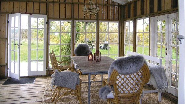 A covered patio with a wooden table, wicker chairs, and a bench with a fur throw. - 3 bedroom awesome home in Mårdaklev (Mårdaklev)