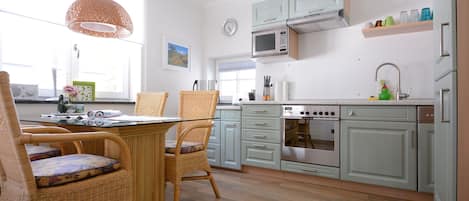 A kitchen with wicker chairs, a dining table, a microwave, and a stove.