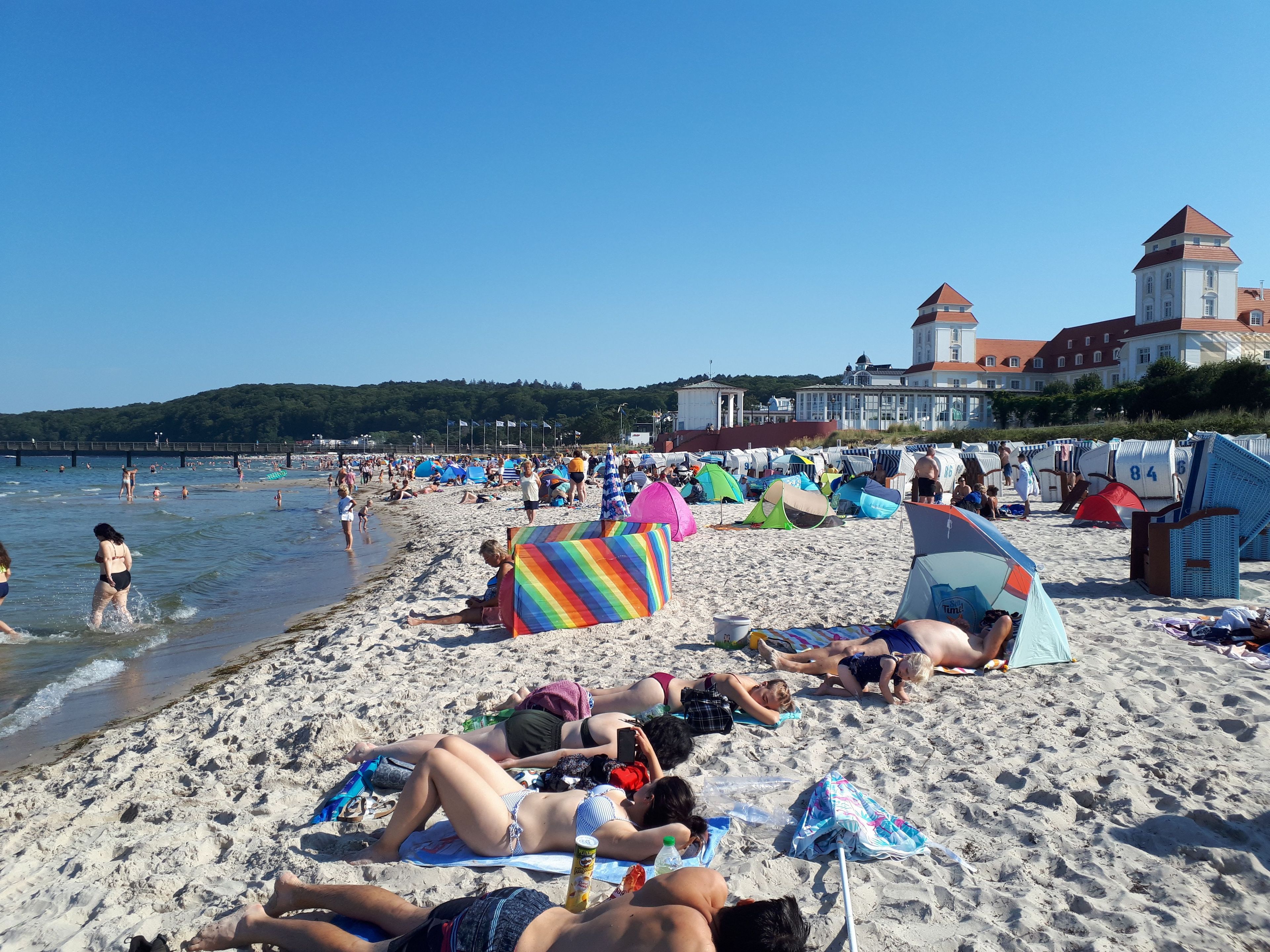 A beach with tents, people sunbathing, and a building in the background.