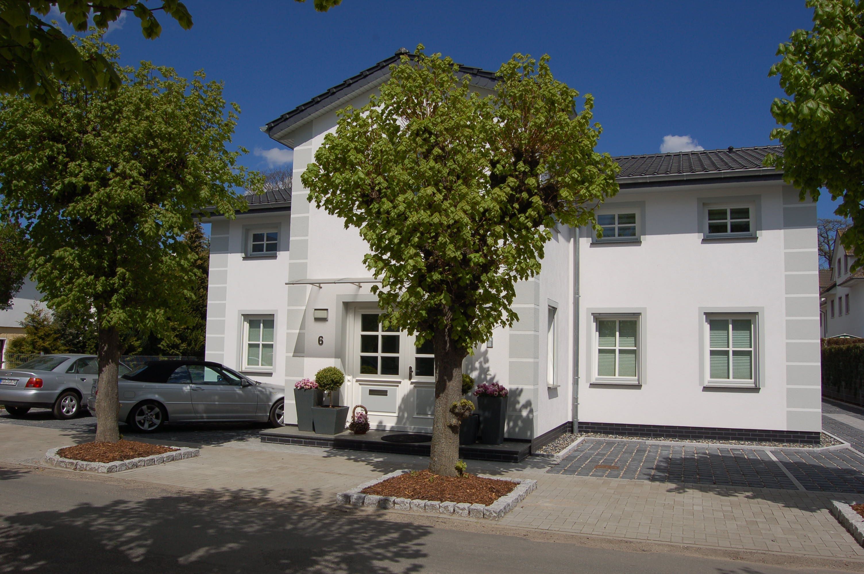 Ein weißes Gebäude mit Baum davor, ein Auto auf der Straße und ein klarer, blauer Himmel.