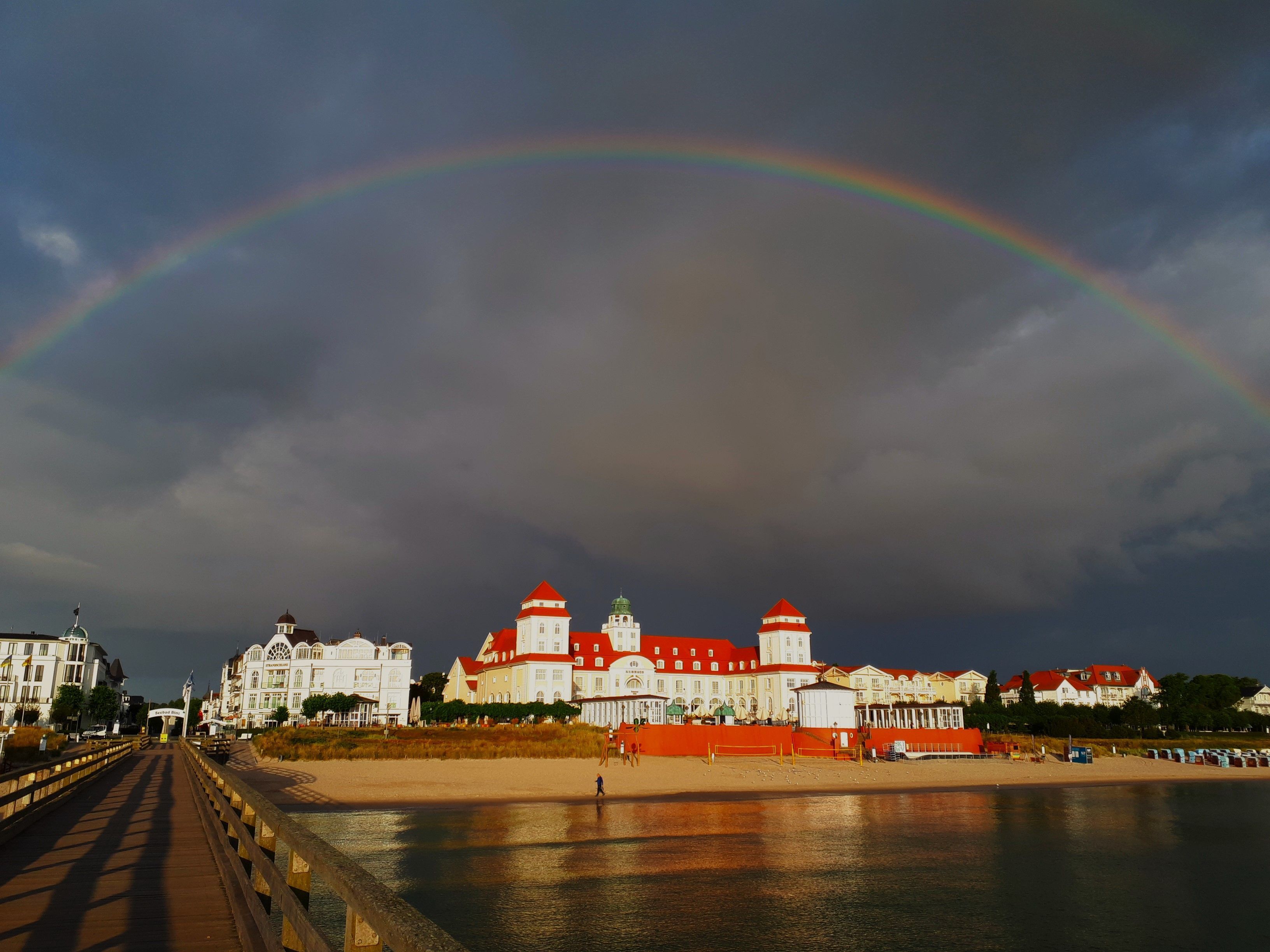 Eine Küstenansicht mit Regenbogen, Brücke und Häusern mit roten Dächern.