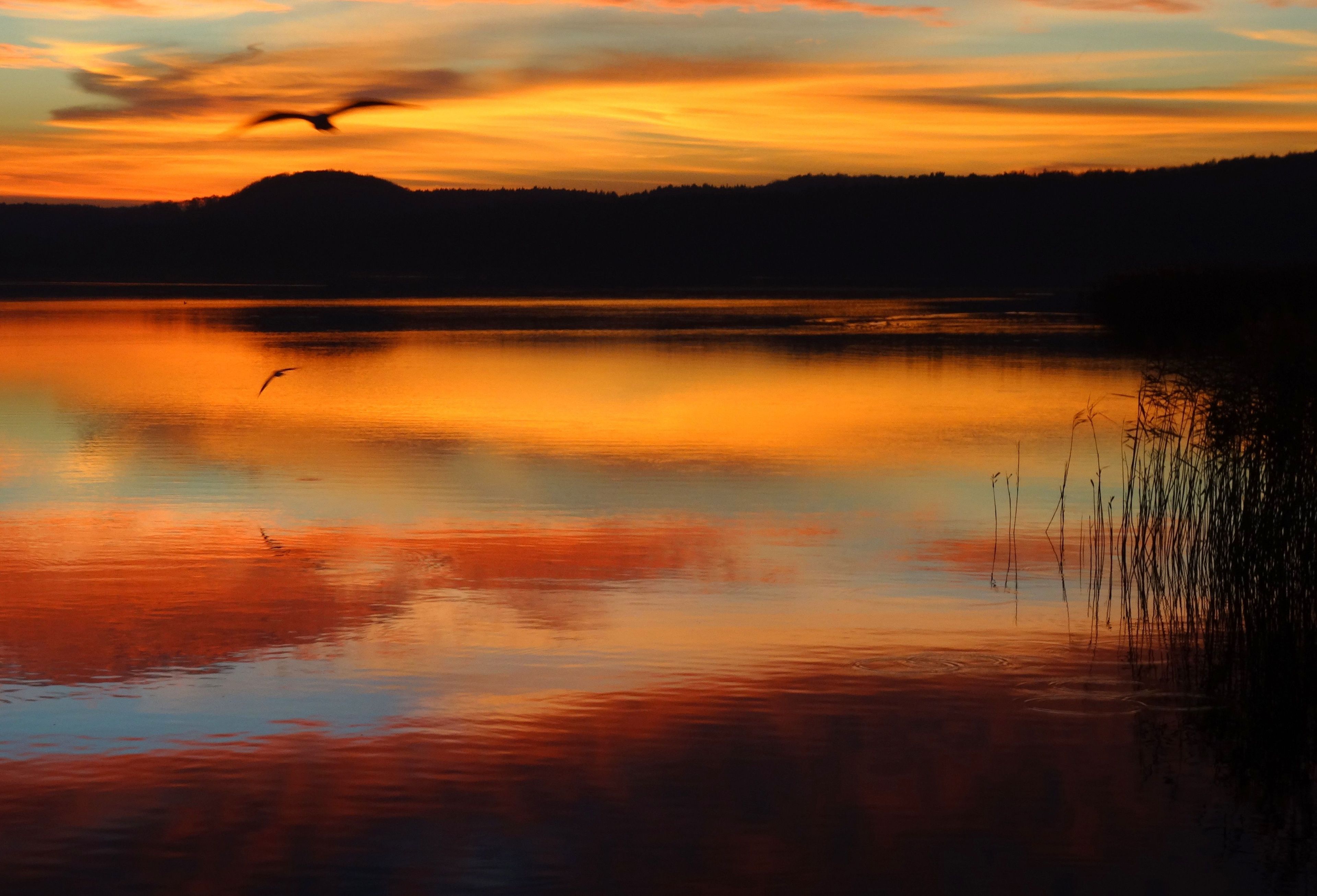 A calm lake at sunset with silhouettes of hills in the background.