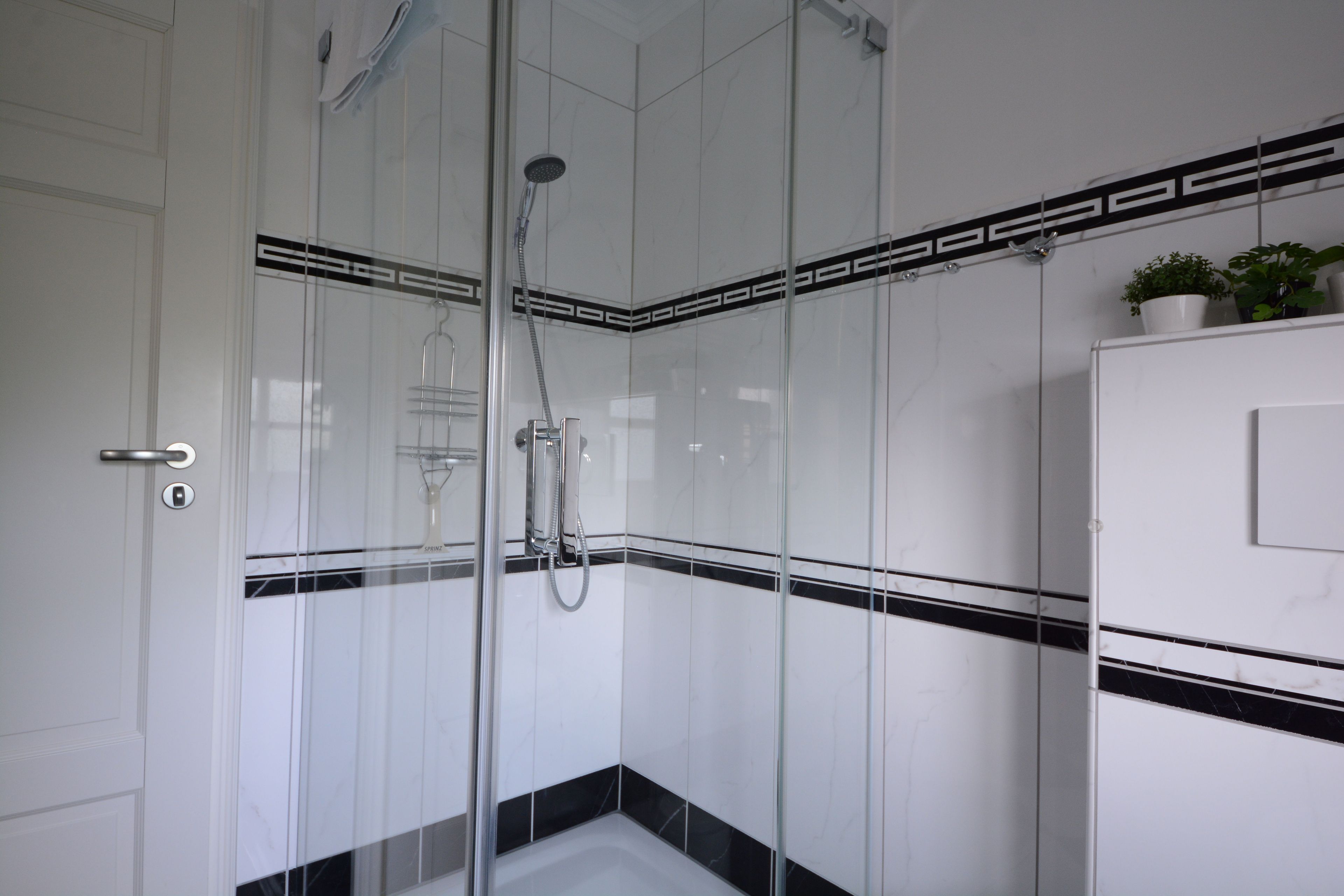 A modern bathroom with a glass-enclosed shower, white tiled walls, and a black decorative border.