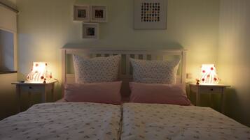 Ein Doppelbett mit Blumenmuster auf der Bettwäsche, zwei Nachttische mit Lampen, ein weißes Kopfteil und gerahmte Bilder an der Wand.