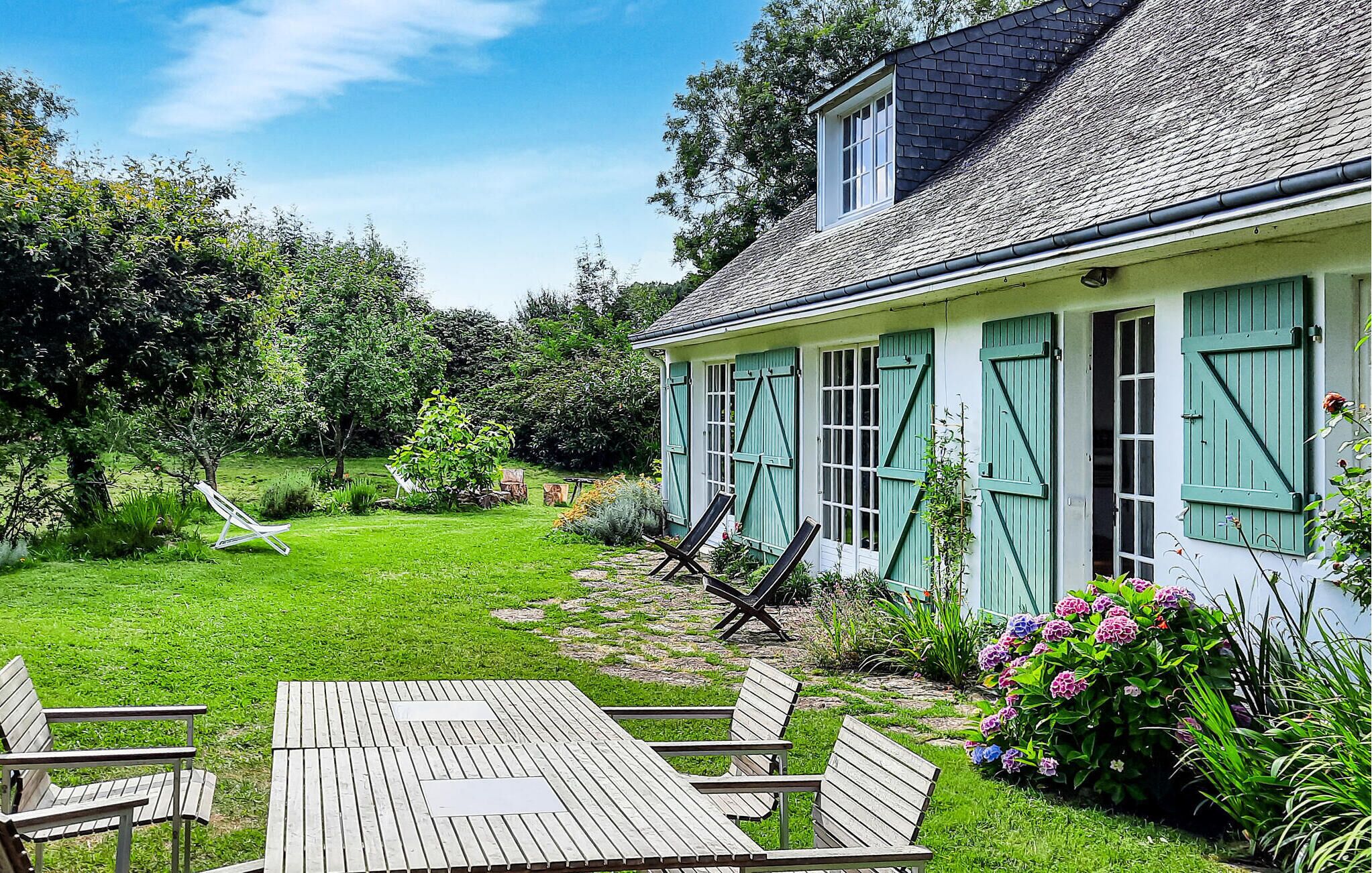 Ein Haus mit Garten, einem Holztisch und zwei Liegestühlen.
