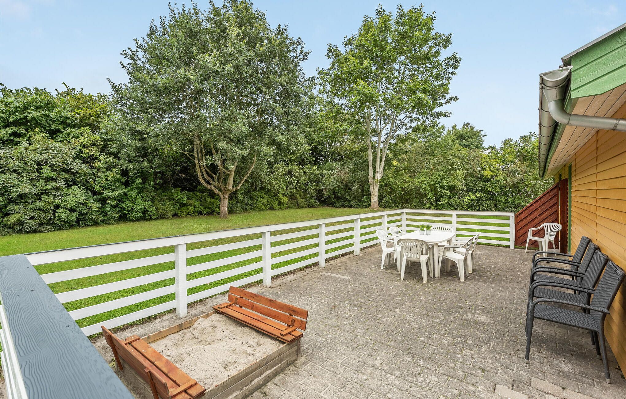 Un espace patio agrémenté d’une clôture blanche, d’un banc en bois et de mobilier d’extérieur.