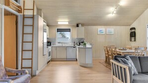 Et rummeligt køkken med træskabe, et spiseområde med bord og stole, samt et sovehems med stige.