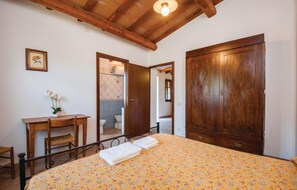 Une chambre à coucher avec un lit, une armoire en bois, un bureau et une petite salle de bain visible à travers une porte ouverte.