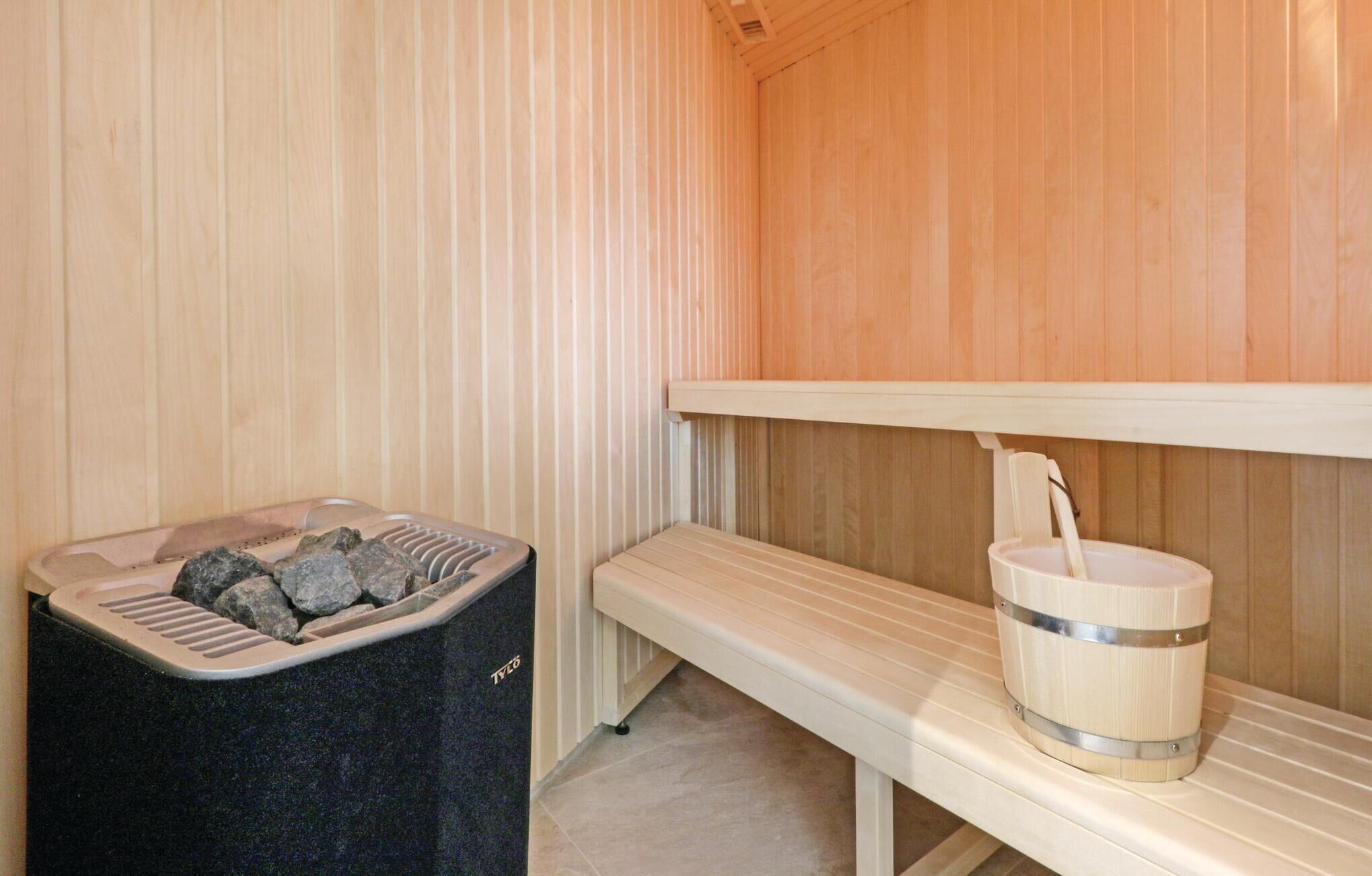 Et sauna-rum med bænk, spand og skraldespand med sten.