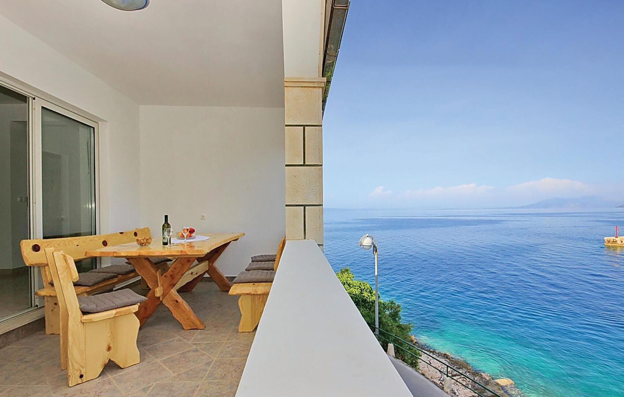 A balcony with a wooden table and chairs, a lamp, and a view of the sea.