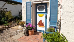 A building with a white exterior, a blue door with a sun and sailboat design, and blue shutters.
