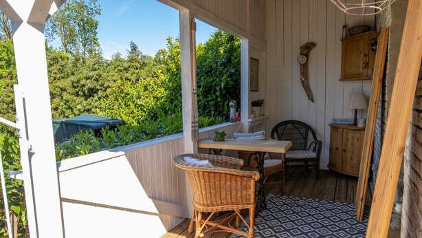 A covered outdoor seating area with a table and chairs, a patterned rug, and a view of greenery.