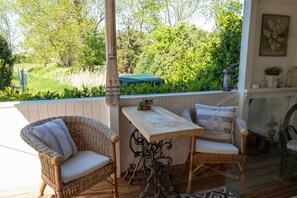 Un porche cubierto con mobiliario de mimbre y una mesa, con vistas a un jardín exuberante.