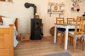 Una habitación acogedora con una cama, una mesa de madera con sillas, una estufa negra y estanterías con diversos objetos.
