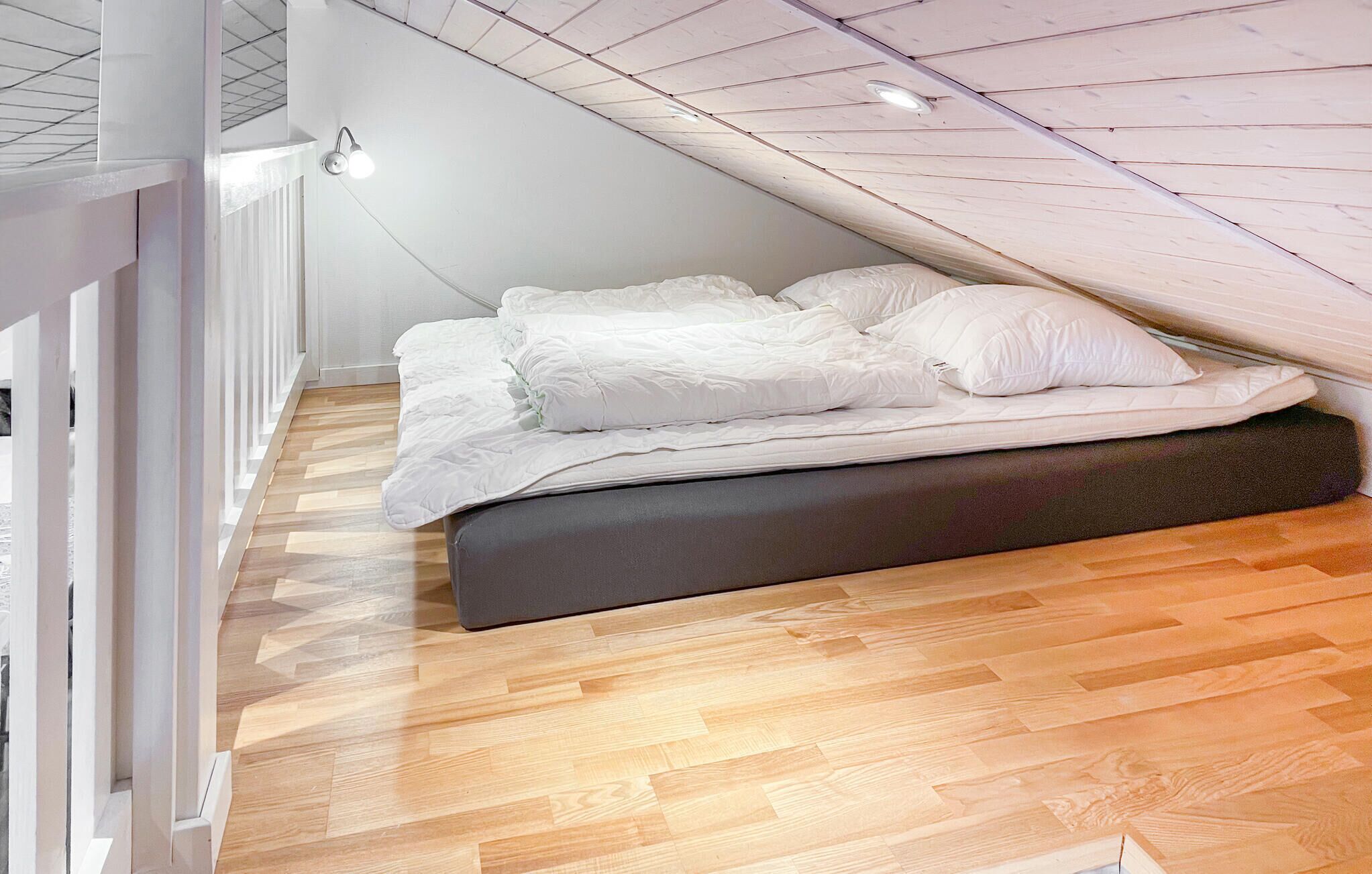 Une chambre avec un lit en mezzanine, un plancher en bois et un plafond en pente.