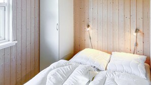 Une chambre à coucher avec une tête de lit en bois, un lit avec une literie blanche et une fenêtre avec un rideau.