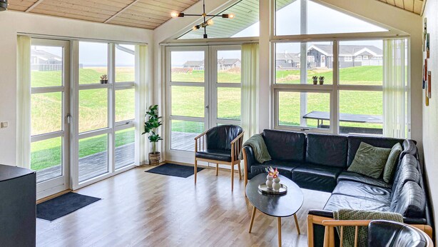 Une pièce spacieuse avec une grande fenêtre, un canapé en cuir noir, une table basse en bois et une plante en pot.